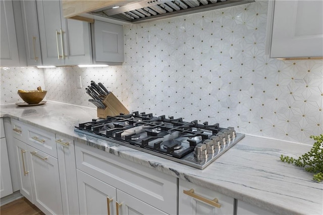 3899 Carlton Dr, Chamblee, GA 30341 - kitchen with stainless steel gas cooktop, wall chimney range hood, decorative backsplash, white cabinetry, and light stone countertops