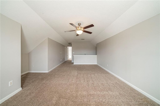 bonus room with baseboards, a ceiling fan, light colored carpet, vaulted ceiling, and a textured ceiling