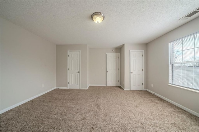 unfurnished bedroom featuring light carpet, a textured ceiling, visible vents, and baseboards