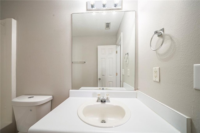 bathroom with toilet, a textured wall, visible vents, and vanity