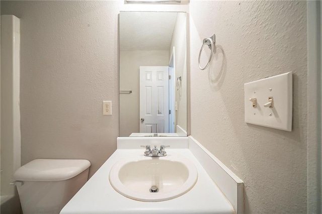 bathroom featuring toilet, a textured wall, and vanity