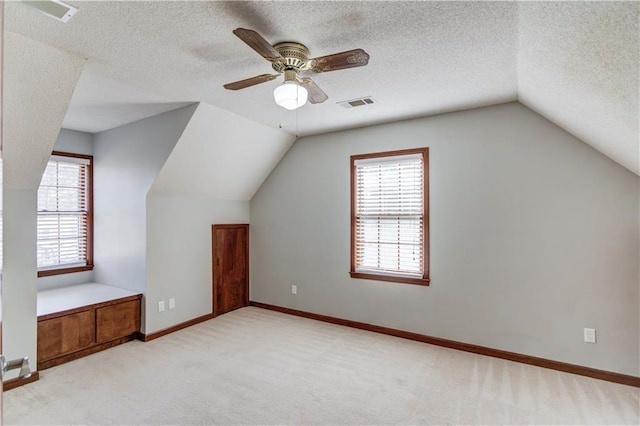 additional living space with vaulted ceiling, light colored carpet, ceiling fan, and a textured ceiling