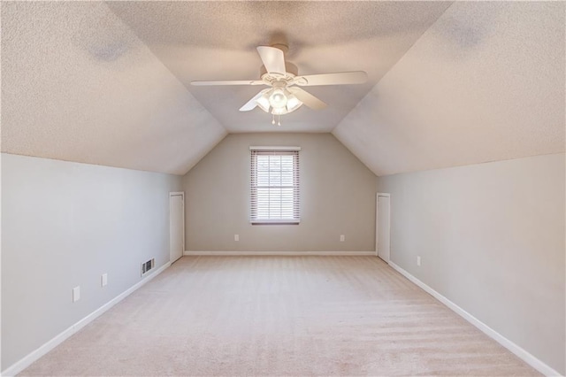 additional living space with ceiling fan, lofted ceiling, light carpet, and a textured ceiling