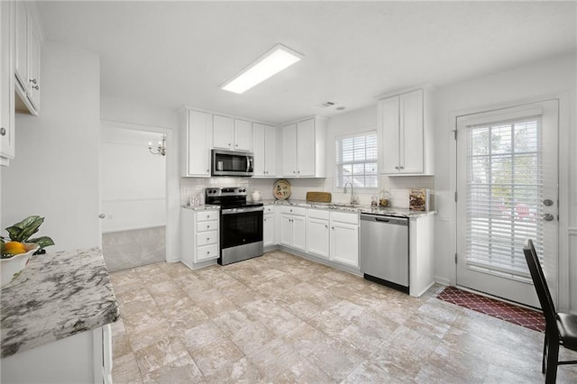 kitchen featuring tasteful backsplash, white cabinetry, light stone counters, a sink, and stainless steel appliances