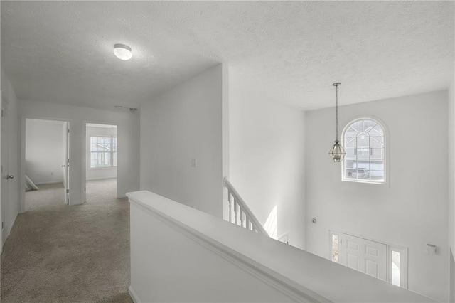 hallway featuring an upstairs landing, carpet, and a textured ceiling