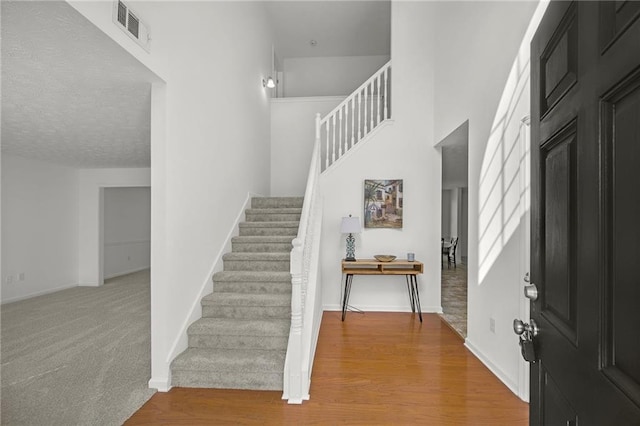 foyer entrance featuring wood finished floors, baseboards, visible vents, and stairs