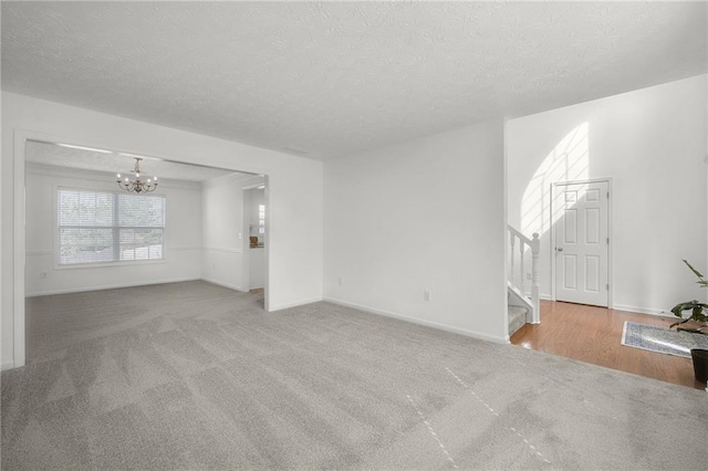 unfurnished living room featuring baseboards, a chandelier, a textured ceiling, stairs, and carpet