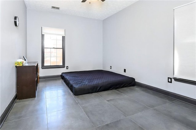 unfurnished bedroom featuring visible vents, ceiling fan, a textured ceiling, tile patterned flooring, and baseboards