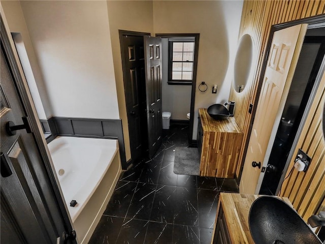 bathroom featuring baseboards, toilet, marble finish floor, vanity, and a bath