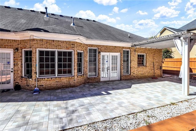 back of property with a shingled roof, french doors, brick siding, and fence