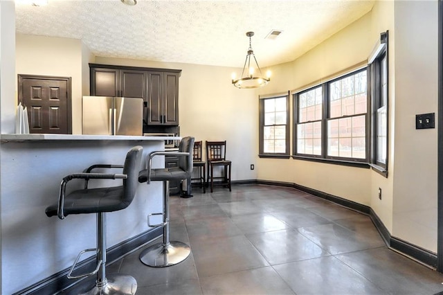 kitchen with baseboards, a kitchen bar, visible vents, and freestanding refrigerator