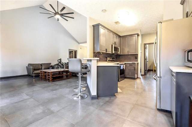 kitchen with high vaulted ceiling, a breakfast bar area, a peninsula, appliances with stainless steel finishes, and backsplash