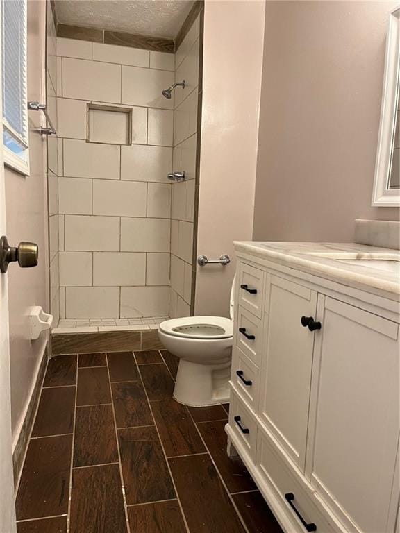 bathroom with a tile shower, vanity, a textured ceiling, and toilet