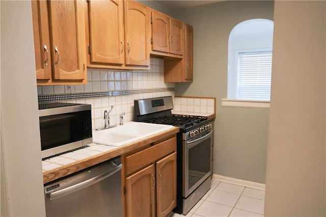 kitchen featuring tile counters, sink, decorative backsplash, light tile patterned floors, and appliances with stainless steel finishes