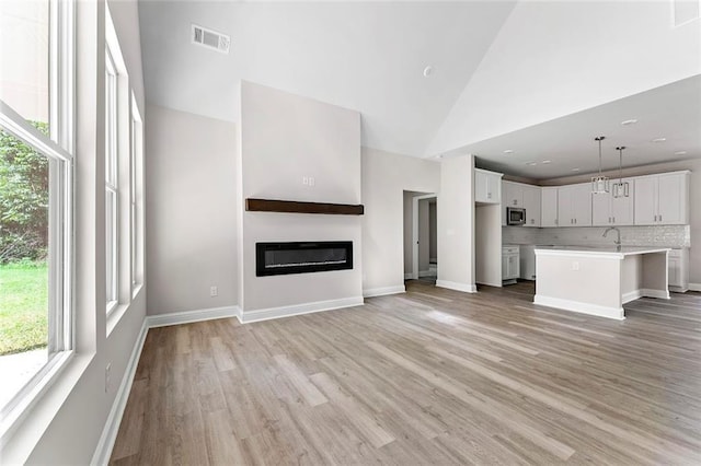 unfurnished living room featuring high vaulted ceiling, sink, and light hardwood / wood-style flooring