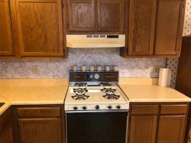 kitchen with ventilation hood, gas stove, light countertops, and brown cabinets