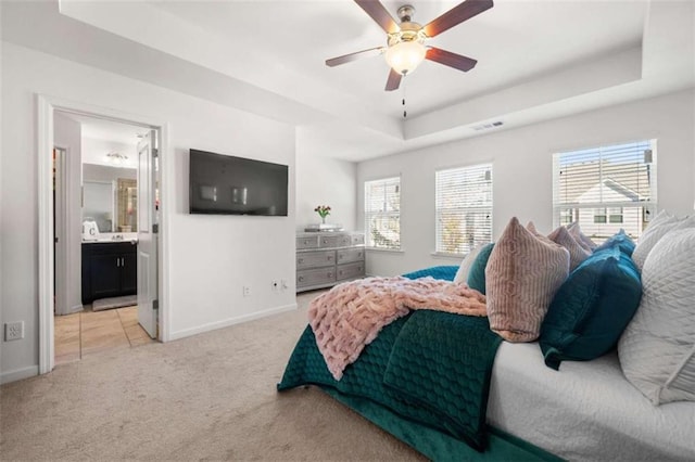 carpeted bedroom with ceiling fan, a raised ceiling, and ensuite bath