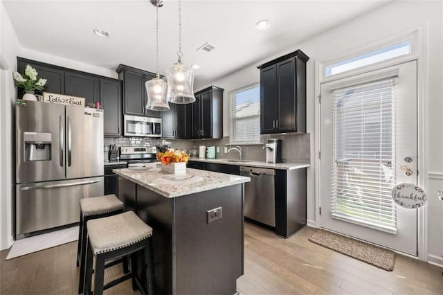 kitchen featuring decorative light fixtures, stainless steel appliances, a kitchen island, and plenty of natural light