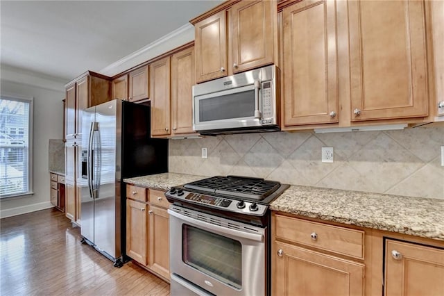 kitchen featuring decorative backsplash, ornamental molding, light stone countertops, stainless steel appliances, and light wood-style floors