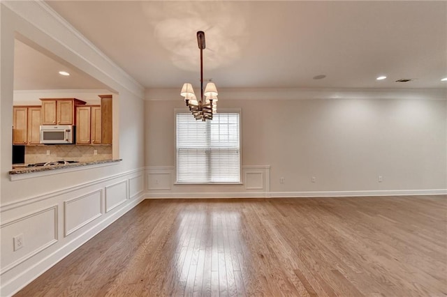 unfurnished dining area with a chandelier, light wood-type flooring, a decorative wall, visible vents, and ornamental molding