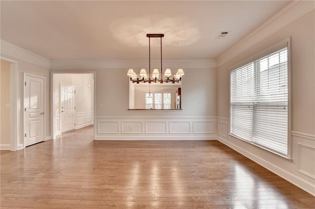 unfurnished dining area with crown molding, light wood-style flooring, a chandelier, visible vents, and a decorative wall