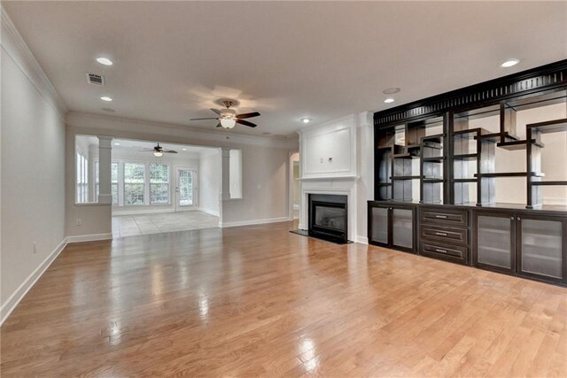 unfurnished living room with visible vents, crown molding, ceiling fan, wood finished floors, and a glass covered fireplace