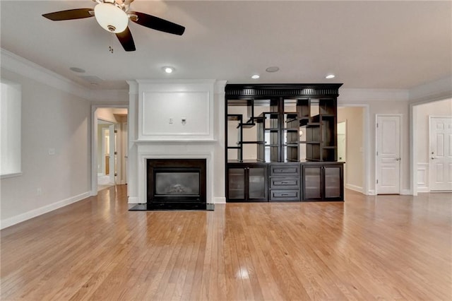unfurnished living room featuring baseboards, ornamental molding, wood finished floors, a fireplace, and a ceiling fan