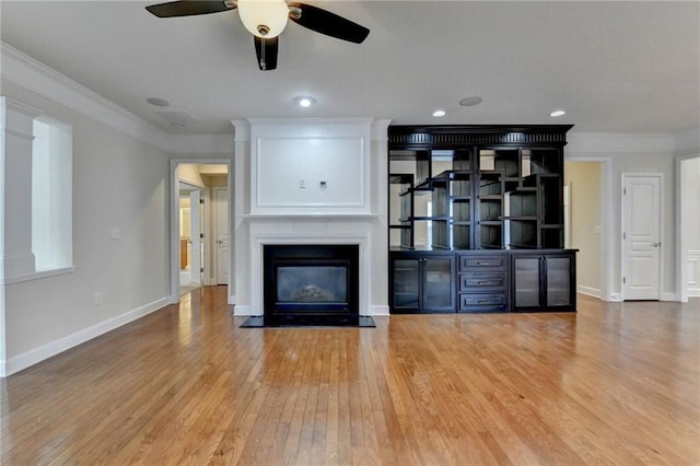 unfurnished living room featuring a fireplace with flush hearth, ceiling fan, wood finished floors, and ornamental molding