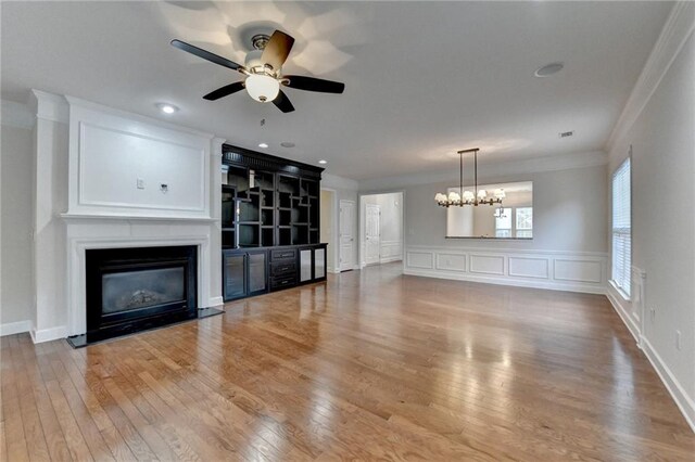unfurnished living room with wood-type flooring, ornamental molding, a fireplace with flush hearth, and ceiling fan with notable chandelier