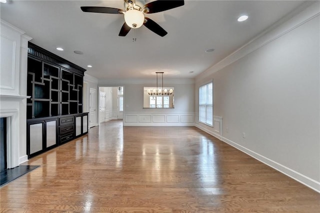 unfurnished living room featuring crown molding, a premium fireplace, light wood-type flooring, ceiling fan with notable chandelier, and a decorative wall