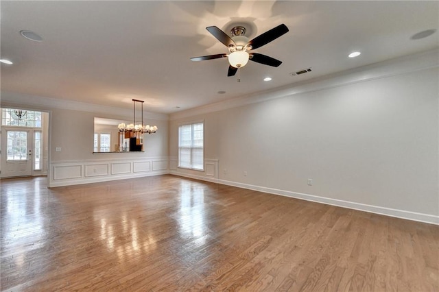 unfurnished room featuring a decorative wall, visible vents, ornamental molding, wood finished floors, and ceiling fan with notable chandelier