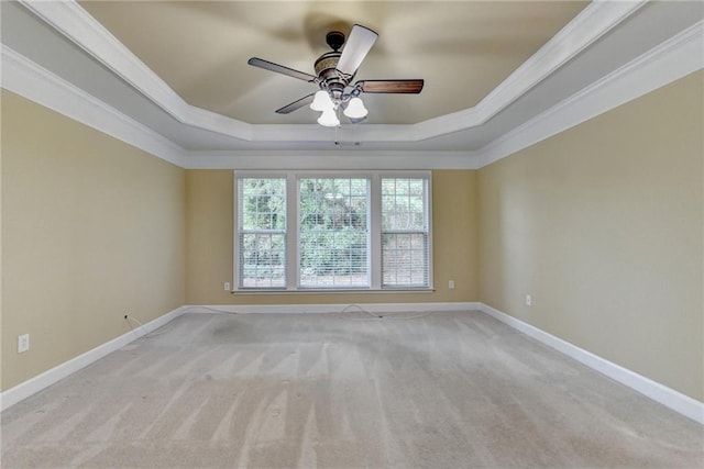 carpeted spare room featuring a raised ceiling, crown molding, baseboards, and ceiling fan