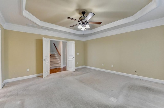 empty room with crown molding, baseboards, ceiling fan, a tray ceiling, and light colored carpet