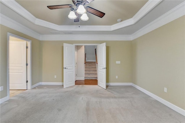 unfurnished bedroom featuring a tray ceiling, light colored carpet, baseboards, and ornamental molding