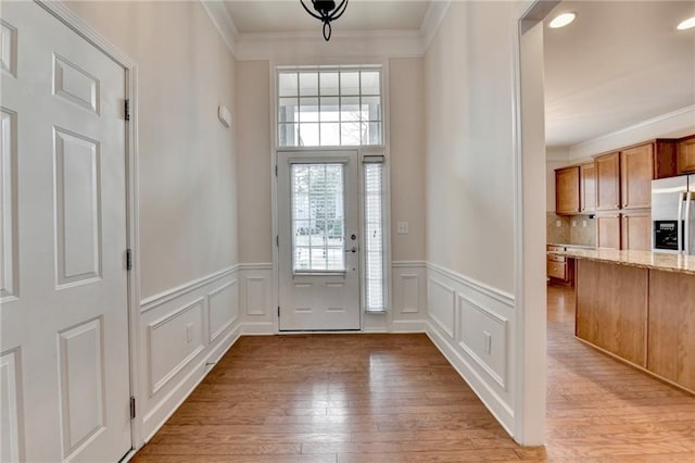entryway featuring a wainscoted wall, ornamental molding, a decorative wall, and light wood-style floors