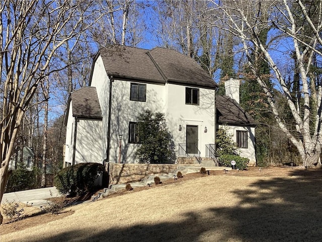 view of front of house with stucco siding, a chimney, and roof with shingles