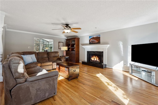 living area with a textured ceiling, ceiling fan, a premium fireplace, and light wood-style flooring