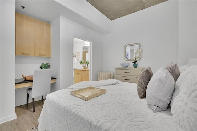 bedroom featuring baseboards, built in study area, light wood finished floors, and ensuite bathroom