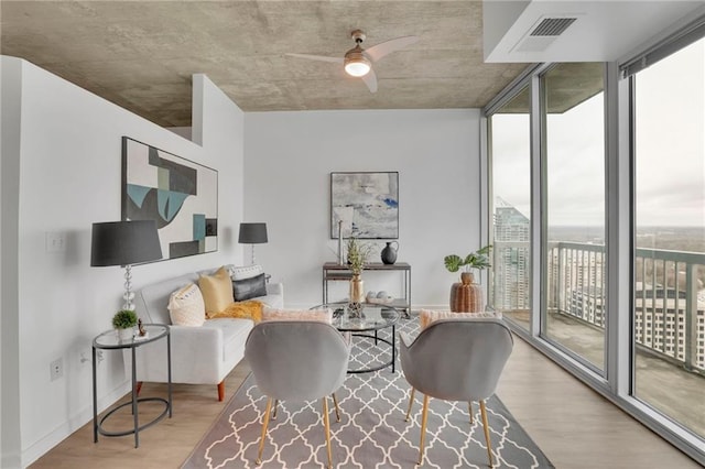 sitting room with expansive windows, wood finished floors, a ceiling fan, and baseboards