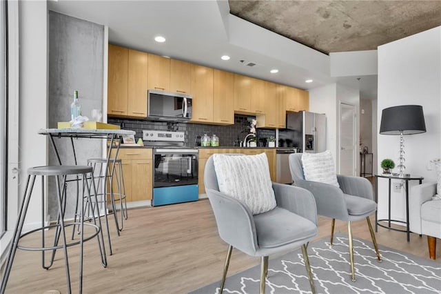 kitchen featuring light wood finished floors, appliances with stainless steel finishes, backsplash, and light brown cabinets