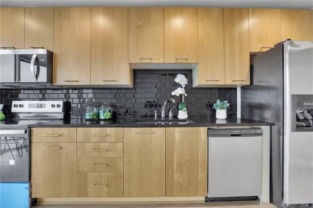 kitchen with stainless steel appliances, a sink, light brown cabinetry, tasteful backsplash, and dark countertops