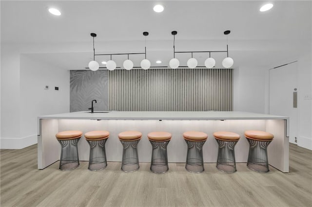 bar with light wood-style flooring, recessed lighting, a sink, indoor wet bar, and decorative light fixtures