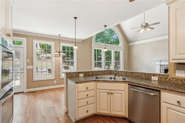 kitchen with sink, decorative light fixtures, dark stone countertops, appliances with stainless steel finishes, and light hardwood / wood-style floors