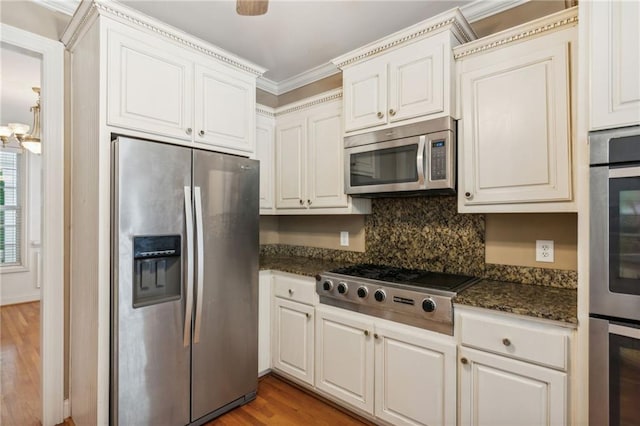 kitchen featuring tasteful backsplash, appliances with stainless steel finishes, dark stone counters, hardwood / wood-style floors, and white cabinets