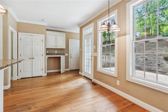 entryway with crown molding, light hardwood / wood-style floors, and a notable chandelier