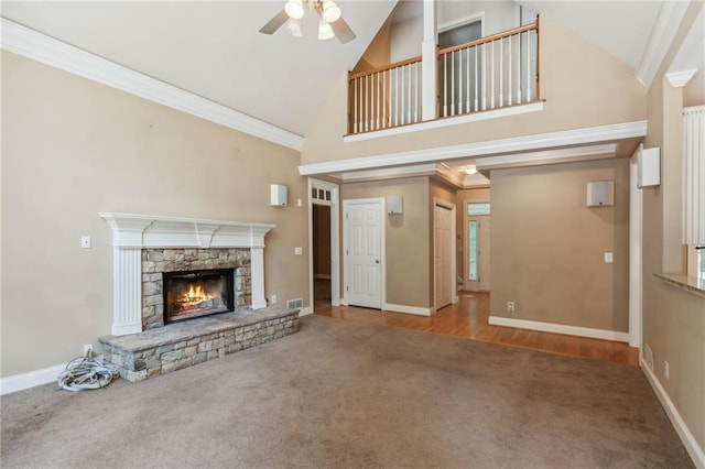 unfurnished living room featuring crown molding, carpet, a stone fireplace, and high vaulted ceiling