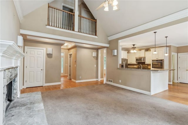 unfurnished living room with ornamental molding, a stone fireplace, light carpet, and ceiling fan