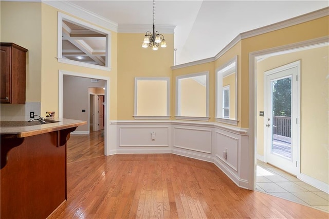 unfurnished dining area featuring beamed ceiling, coffered ceiling, an inviting chandelier, light hardwood / wood-style flooring, and ornamental molding