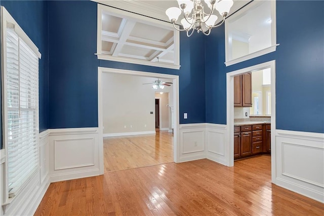 unfurnished dining area featuring coffered ceiling, beamed ceiling, ceiling fan with notable chandelier, and light hardwood / wood-style floors