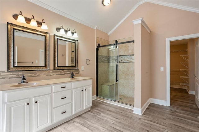 bathroom with vanity, ornamental molding, a shower with shower door, hardwood / wood-style flooring, and vaulted ceiling